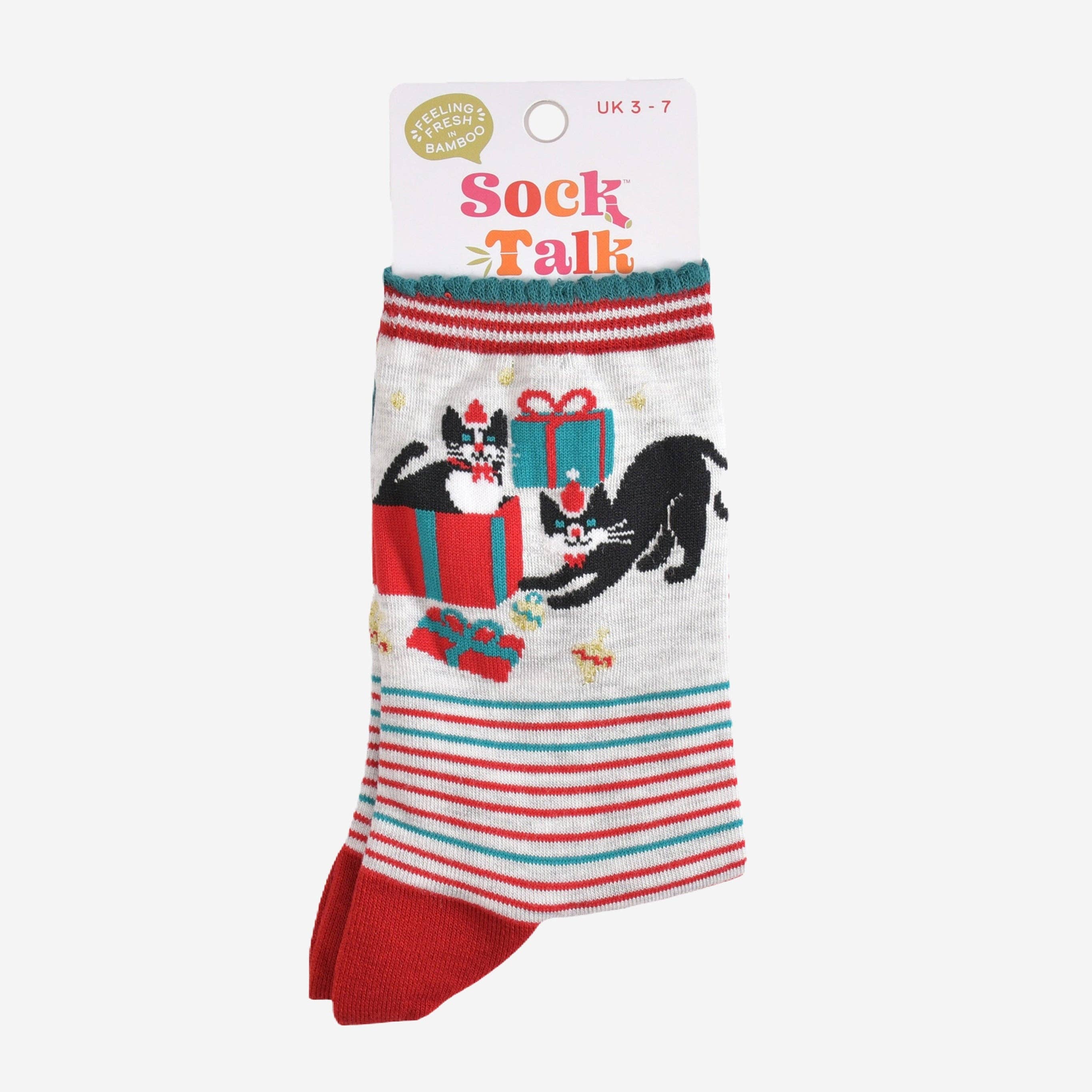 Et par sammenbrettede sokker med kattedesign og julegaver, vist i sin originale emballasje med merkets navn "Sock Talk". Størrelsen og materialet er oppgitt på emballasjen.