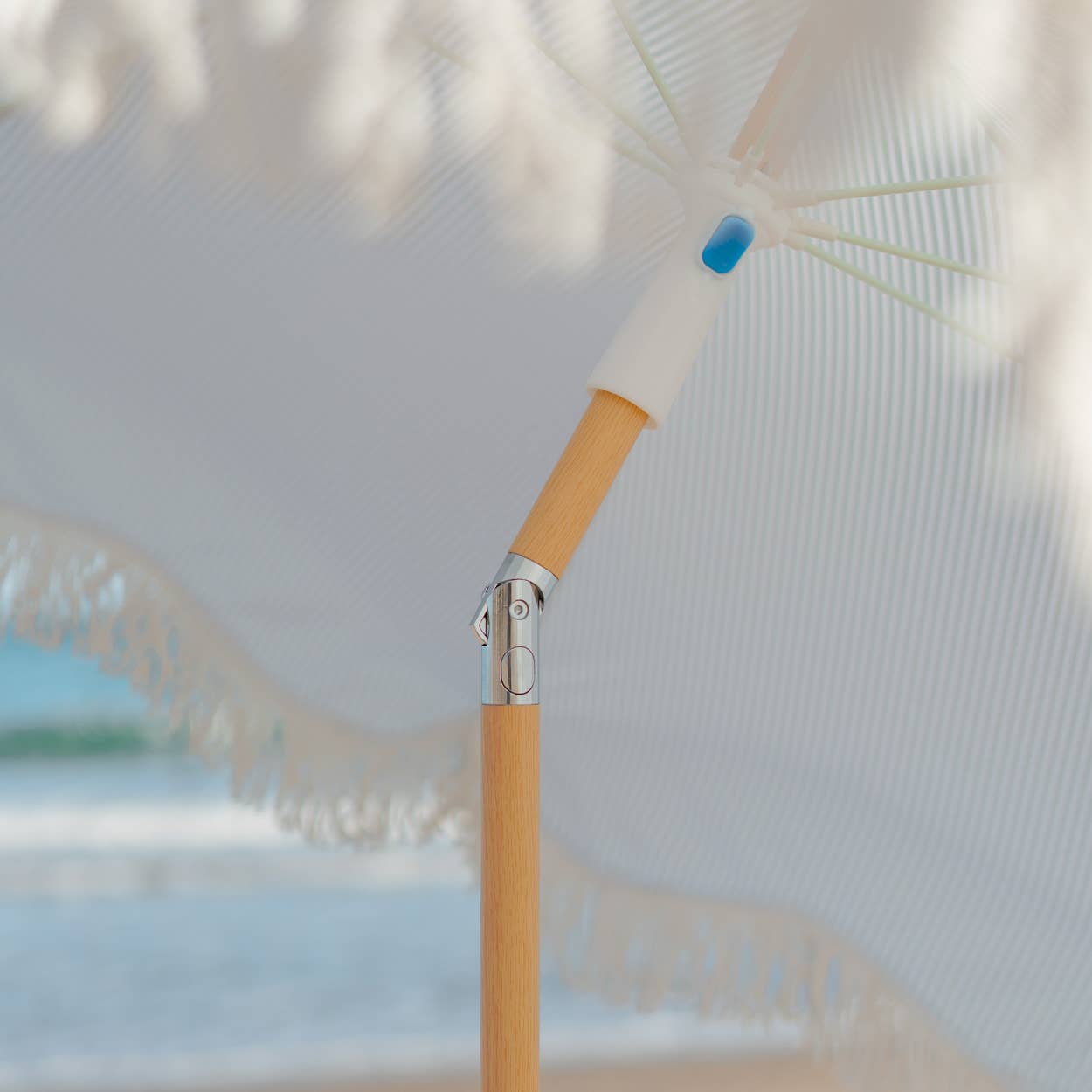 Blå-stripete strandparasoll CAPRI, satt opp på stranden, perfekt for beskyttelse mot solen med en elegant og tidløs stil.