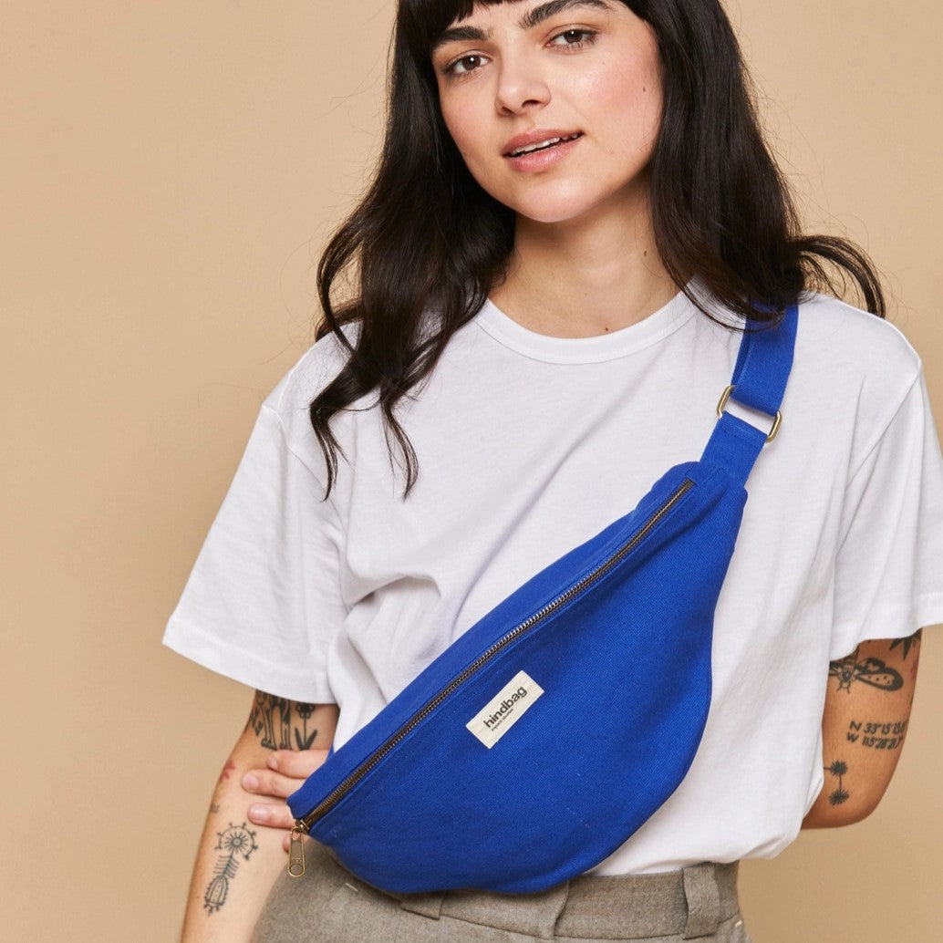 Kvinne med blå Sasha crossbody-veske, iført hvit t-skjorte. Vesken bæres diagonalt over brystet.